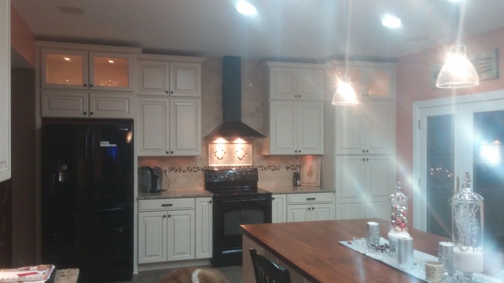 Large transitional kitchen photo with a farmhouse sink, raised-panel cabinets, quartz countertops, beige backsplash, ceramic backsplash, black appliances and an island