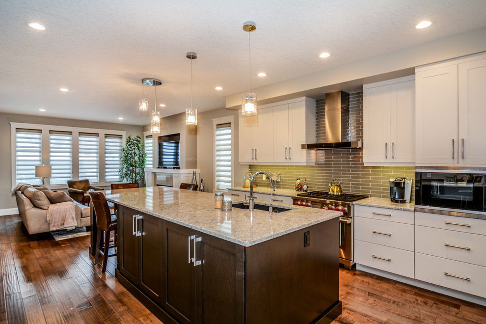 Photo of a large transitional l-shaped open plan kitchen in Calgary with an undermount sink, shaker cabinets, white cabinets, granite benchtops, grey splashback, porcelain splashback, stainless steel appliances, medium hardwood floors and with island.