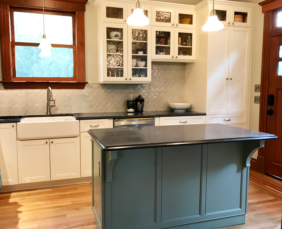 Photo of a mid-sized traditional u-shaped separate kitchen with a farmhouse sink, shaker cabinets, white cabinets, quartz benchtops, grey splashback, ceramic splashback, stainless steel appliances, medium hardwood floors, with island, brown floor and blue benchtop.