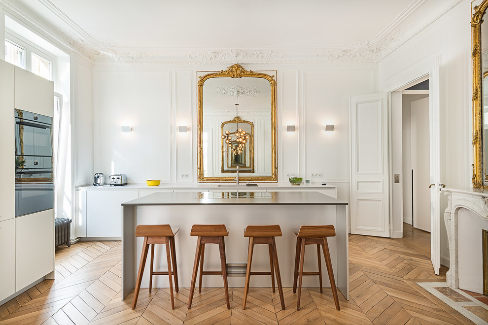 Design ideas for a large traditional galley open plan kitchen in Paris with white cabinets, light hardwood floors, flat-panel cabinets, with island, white splashback and timber splashback.