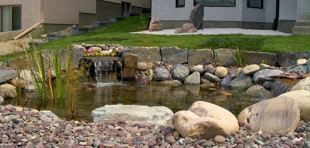 Inspiration for a mid-sized modern backyard partial sun formal garden in Calgary with with pond and natural stone pavers.