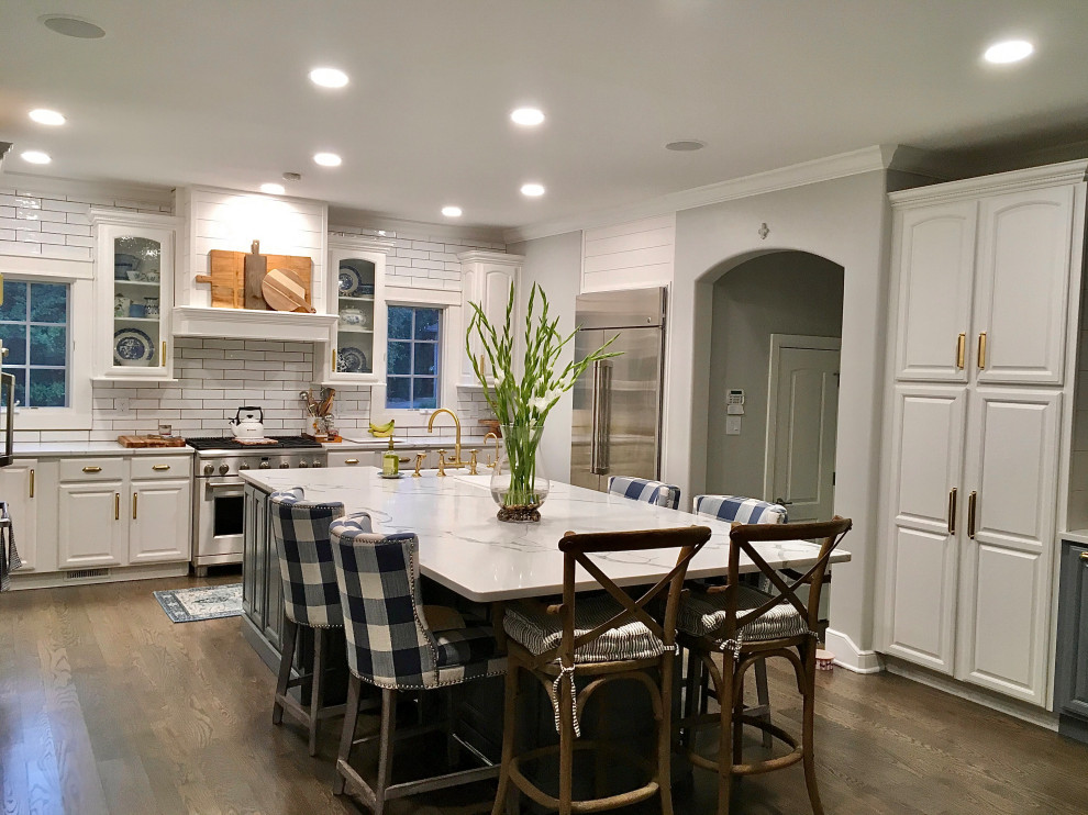 Photo of a mid-sized country eat-in kitchen in Indianapolis with a farmhouse sink, raised-panel cabinets, white cabinets, quartz benchtops, stainless steel appliances, with island, brown floor and multi-coloured benchtop.