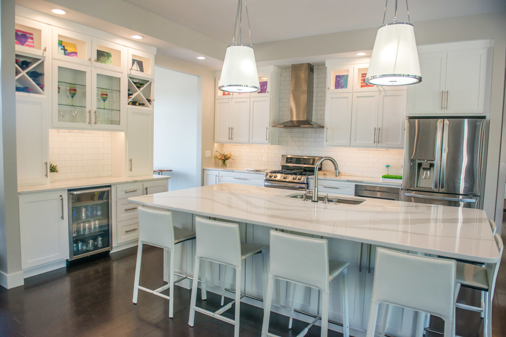Open concept kitchen - huge transitional l-shaped dark wood floor and brown floor open concept kitchen idea with a double-bowl sink, shaker cabinets, white cabinets, quartz countertops, white backsplash, ceramic backsplash, stainless steel appliances and an island