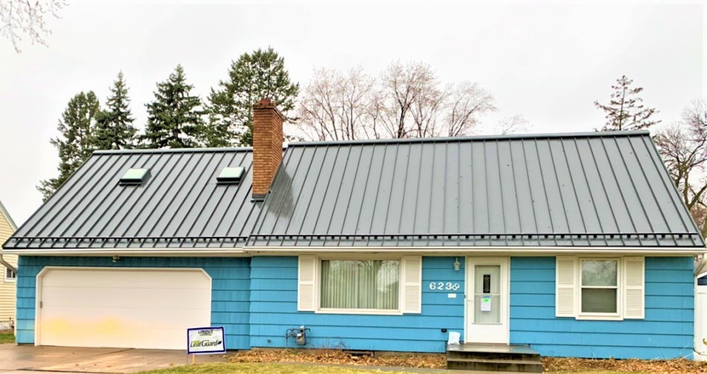 Cette image montre une façade de maison bleue vintage de taille moyenne et de plain-pied avec un toit en métal et un toit gris.