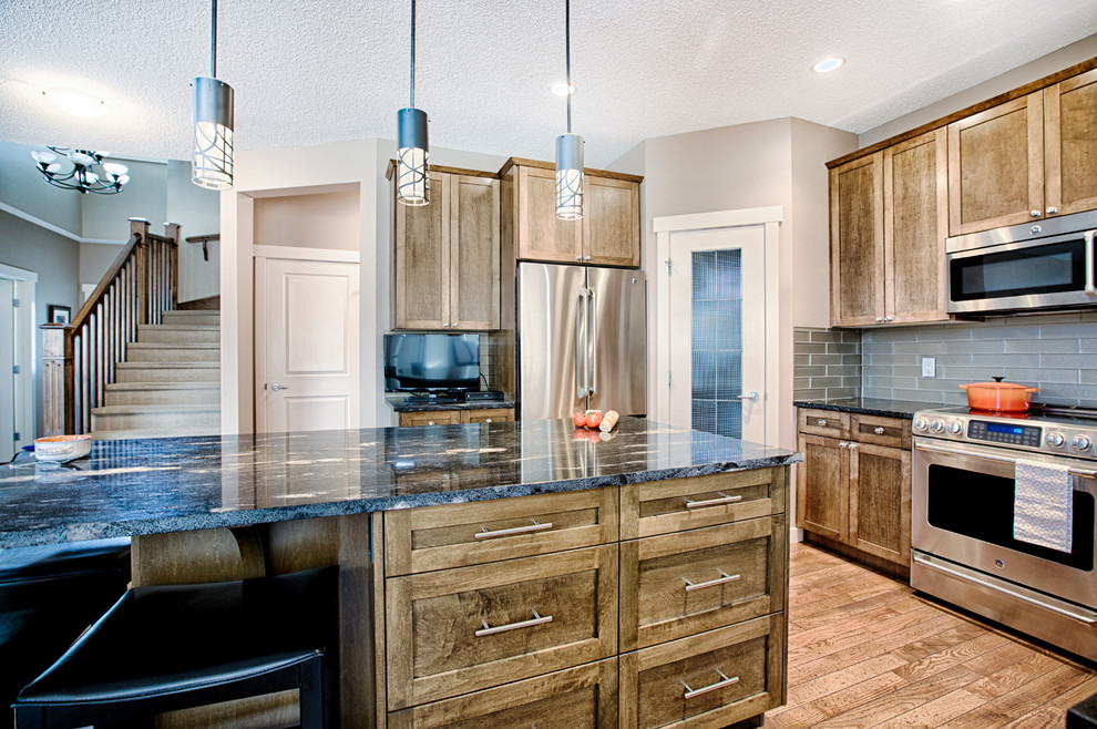 Inspiration for a mid-sized rustic u-shaped medium tone wood floor and brown floor eat-in kitchen remodel in Calgary with an undermount sink, shaker cabinets, medium tone wood cabinets, granite countertops, gray backsplash, glass tile backsplash, stainless steel appliances and an island