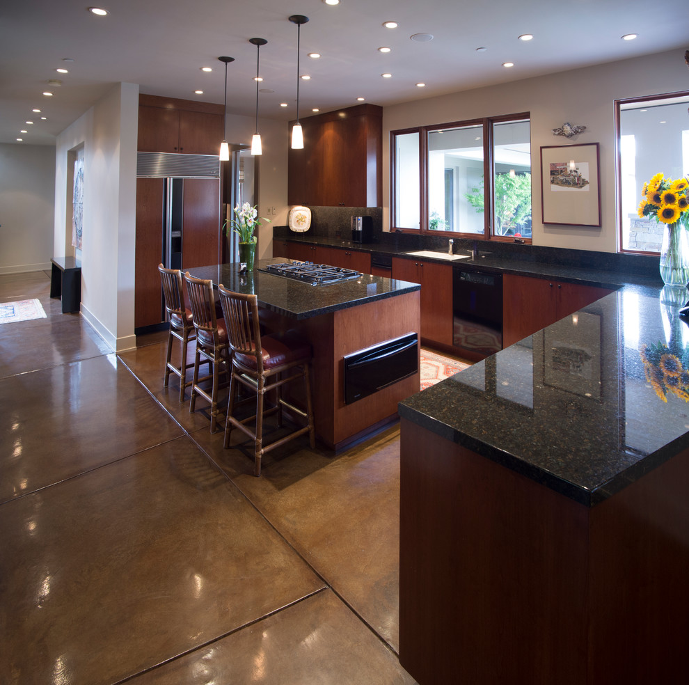This is an example of a mid-sized contemporary open plan kitchen in San Francisco with a single-bowl sink, flat-panel cabinets, dark wood cabinets, granite benchtops, black splashback, black appliances, concrete floors and with island.