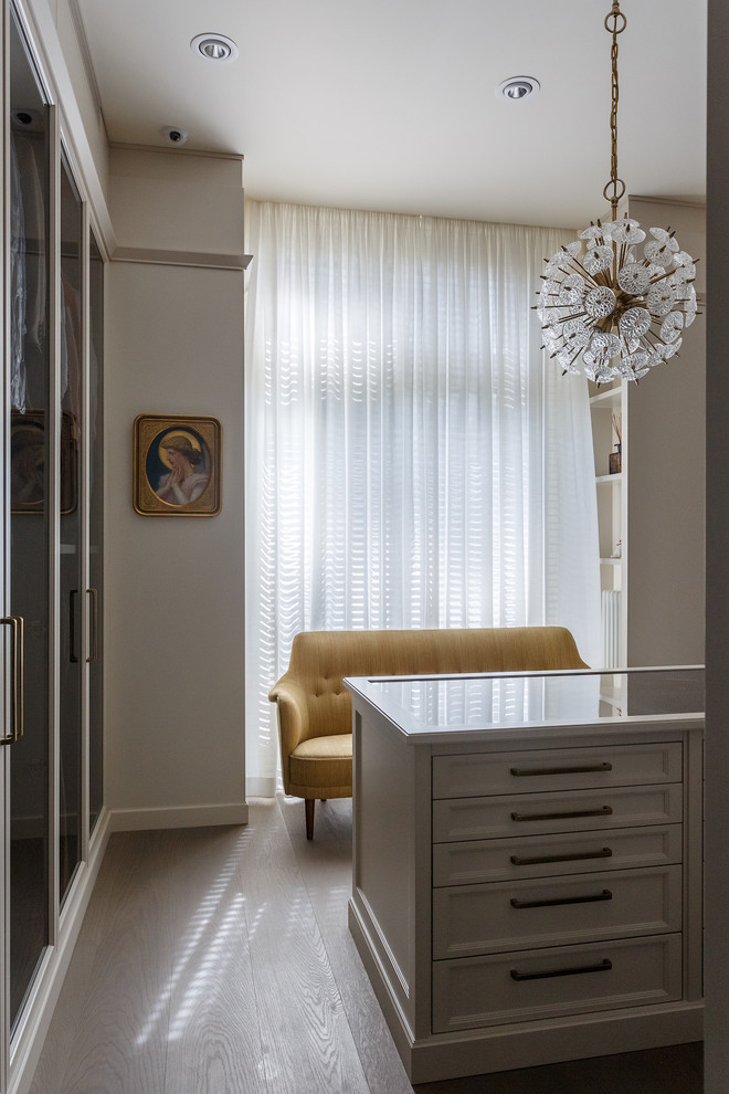 Photo of a traditional women's dressing room in Moscow with white cabinets and light hardwood floors.