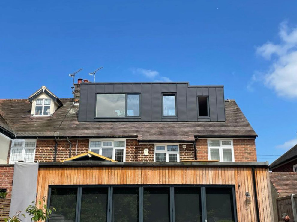 This is an example of a multi-coloured modern rear house exterior in Essex with metal cladding, a pitched roof, a mixed material roof, a black roof and board and batten cladding.