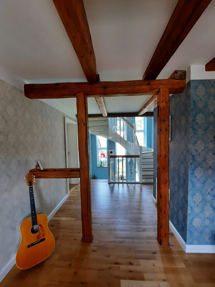 Immagine di un grande ingresso o corridoio country con pavimento in legno massello medio, carta da parati, pareti blu, pavimento marrone e travi a vista