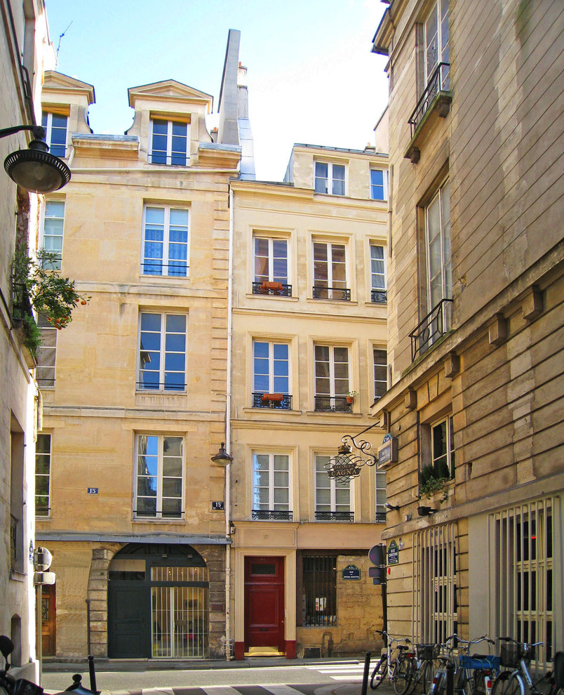 Photo of a mid-sized traditional three-storey beige apartment exterior in Paris with stone veneer and a gable roof.