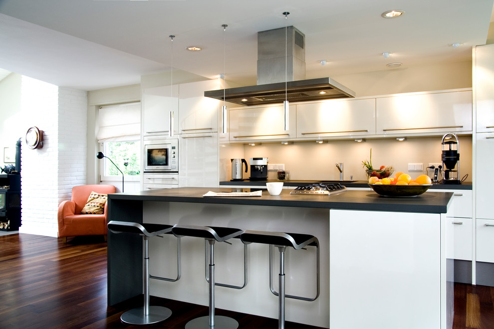 ケルンにある高級な広いコンテンポラリースタイルのおしゃれなキッチン (フラットパネル扉のキャビネット、一体型シンク、白いキャビネット、ベージュキッチンパネル、白い調理設備、濃色無垢フローリング) の写真