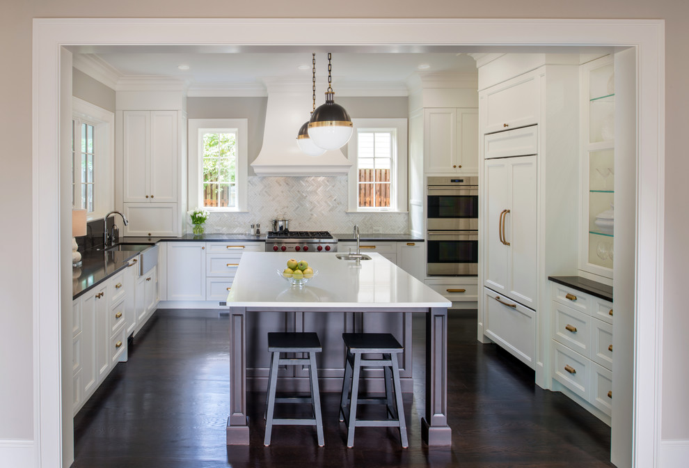 Photo of a large traditional u-shaped eat-in kitchen in DC Metro with a farmhouse sink, recessed-panel cabinets, white cabinets, quartzite benchtops, white splashback, mosaic tile splashback, stainless steel appliances, dark hardwood floors and with island.