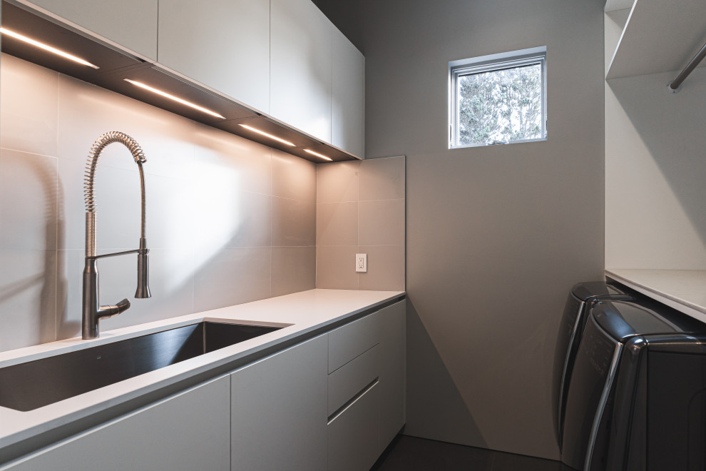 This is an example of a small modern galley dedicated laundry room in Portland with an undermount sink, flat-panel cabinets, white cabinets, quartz benchtops, white walls, ceramic floors, a side-by-side washer and dryer, grey floor and white benchtop.