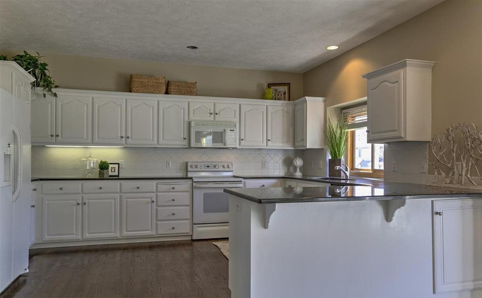 Inspiration for a mid-sized transitional u-shaped dark wood floor eat-in kitchen remodel in Omaha with an undermount sink, shaker cabinets, white cabinets, granite countertops, white backsplash, ceramic backsplash, stainless steel appliances and a peninsula