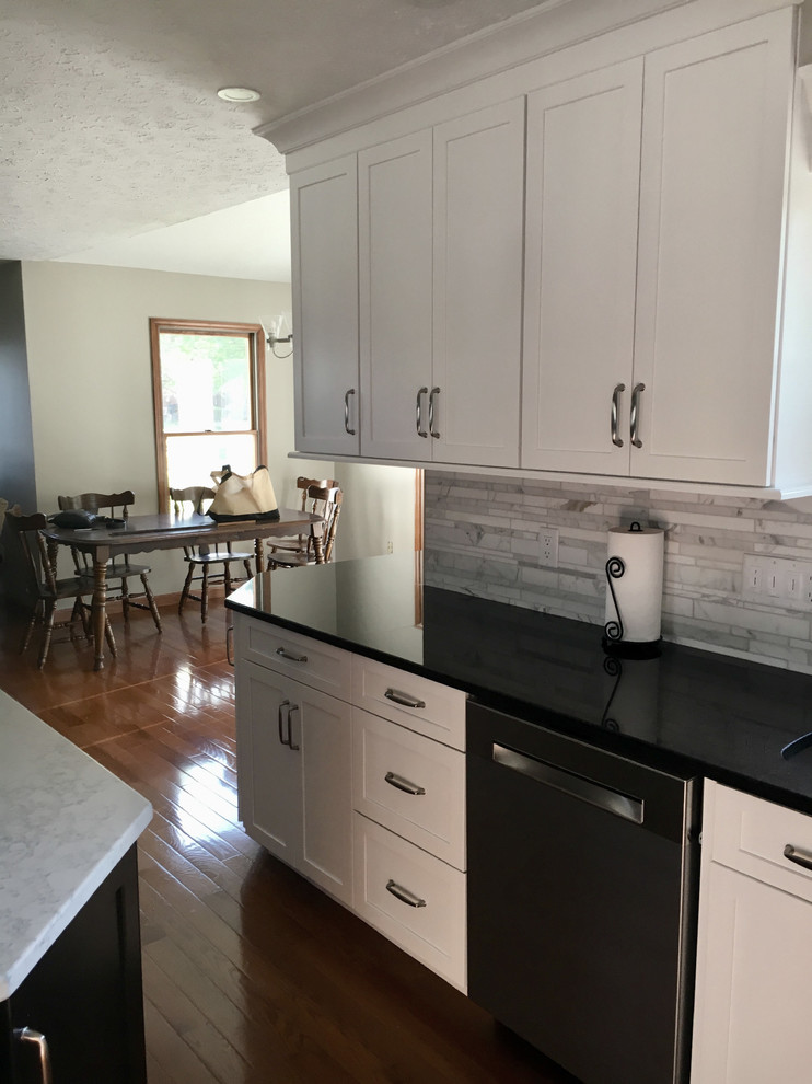 Large transitional single-wall medium tone wood floor eat-in kitchen photo with an undermount sink, shaker cabinets, white cabinets, granite countertops, multicolored backsplash, marble backsplash, stainless steel appliances, an island and black countertops