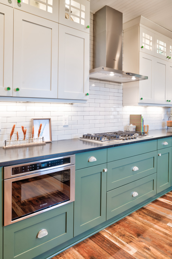 Inspiration for a country u-shaped kitchen/diner in Minneapolis with a belfast sink, shaker cabinets, green cabinets, white splashback, metro tiled splashback, stainless steel appliances, a breakfast bar, brown floors and black worktops.