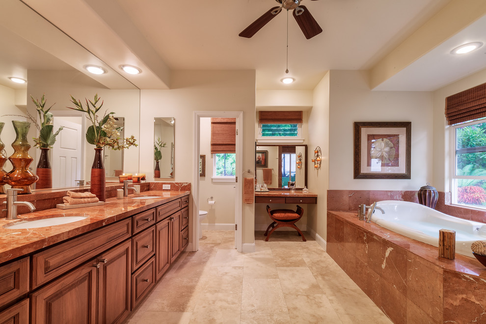 Design ideas for a tropical bathroom in Hawaii with recessed-panel cabinets, marble benchtops, travertine floors, an undermount sink, a drop-in tub and white walls.