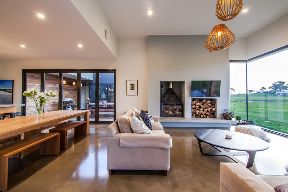 This is an example of a mid-sized contemporary open concept living room in Hobart with white walls, concrete floors, a concrete fireplace surround and a wall-mounted tv.