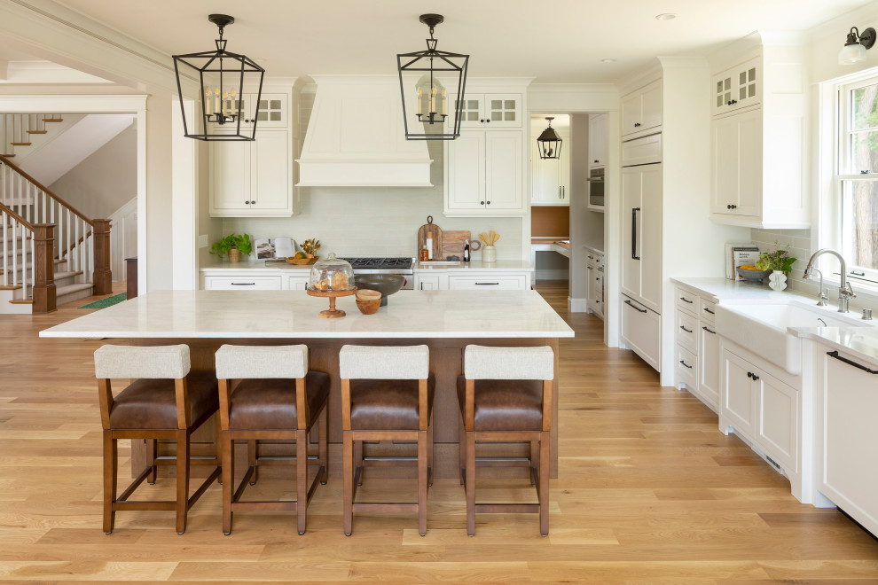 Example of a mid-sized beach style l-shaped light wood floor and coffered ceiling eat-in kitchen design in Minneapolis with a farmhouse sink, beaded inset cabinets, white cabinets, quartz countertops, beige backsplash, ceramic backsplash, stainless steel appliances, an island and white countertops