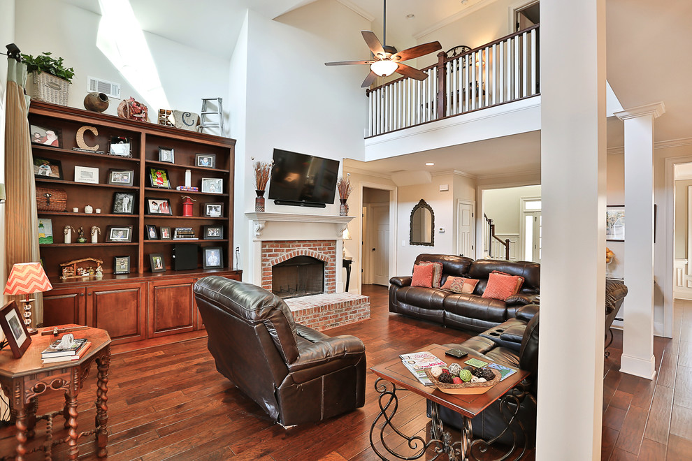 Photo of a mid-sized country open concept family room in Atlanta with white walls, medium hardwood floors, a standard fireplace, a brick fireplace surround and a wall-mounted tv.