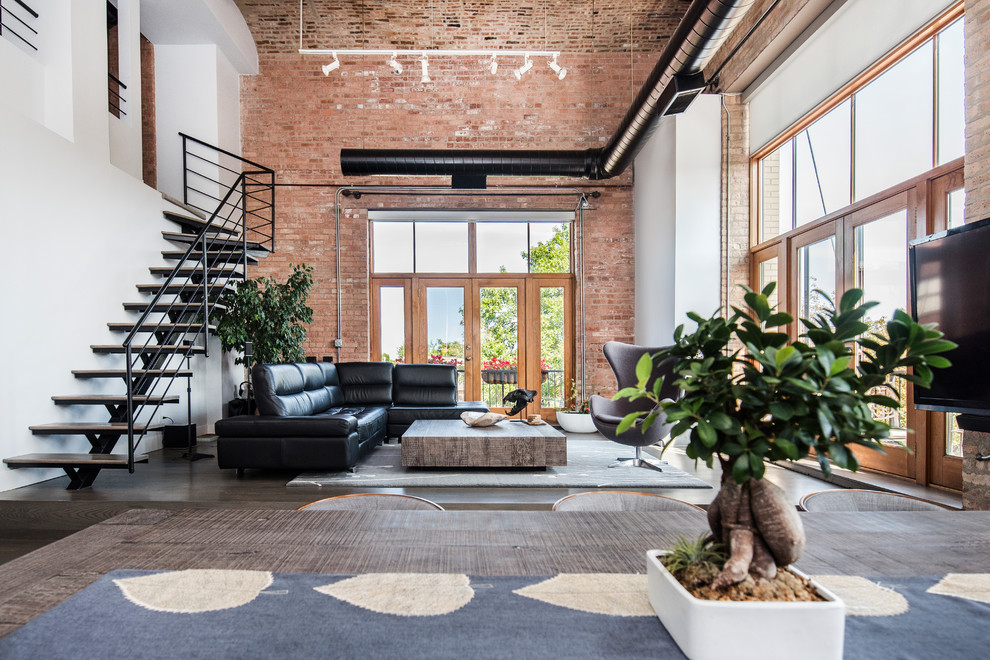 This is an example of an industrial open concept living room in Chicago with white walls, dark hardwood floors and brown floor.