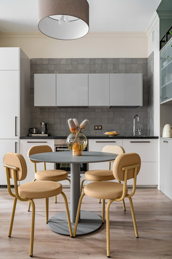 Photo of a small scandinavian single-wall eat-in kitchen in Saint Petersburg with a single-bowl sink, flat-panel cabinets, white cabinets, solid surface benchtops, grey splashback, ceramic splashback, white appliances, laminate floors, no island, beige floor and black benchtop.