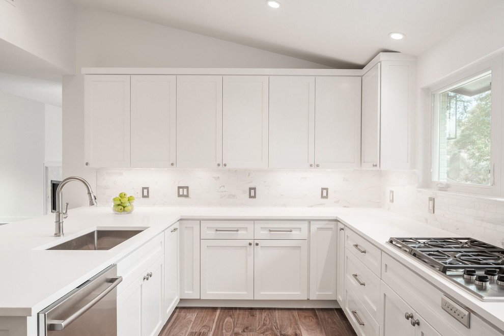 Transitional u-shaped medium tone wood floor enclosed kitchen photo in Austin with a single-bowl sink, shaker cabinets, white cabinets, quartz countertops, white backsplash, stone tile backsplash, stainless steel appliances and a peninsula