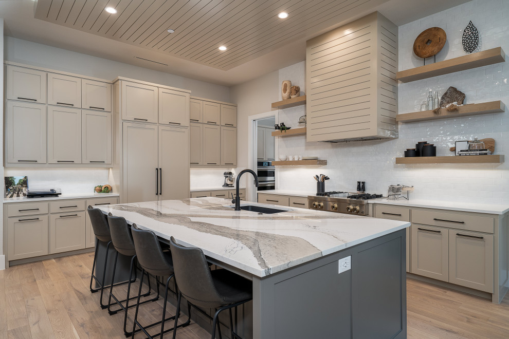 This is an example of a transitional l-shaped kitchen in Dallas with an undermount sink, shaker cabinets, beige cabinets, white splashback, stainless steel appliances, light hardwood floors, with island and white benchtop.