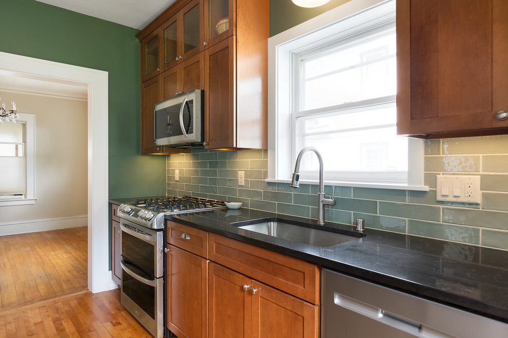 Photo of a small traditional galley separate kitchen in Minneapolis with an undermount sink, shaker cabinets, medium wood cabinets, granite benchtops, green splashback, ceramic splashback, stainless steel appliances, light hardwood floors, brown floor and black benchtop.