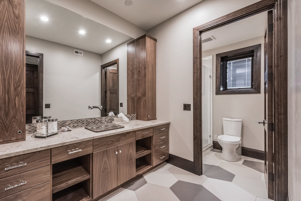 Design ideas for a mid-sized traditional 3/4 bathroom in Salt Lake City with flat-panel cabinets, medium wood cabinets, an alcove shower, beige walls, porcelain floors, a drop-in sink, a hinged shower door, a one-piece toilet, beige tile, glass tile, limestone benchtops and multi-coloured floor.