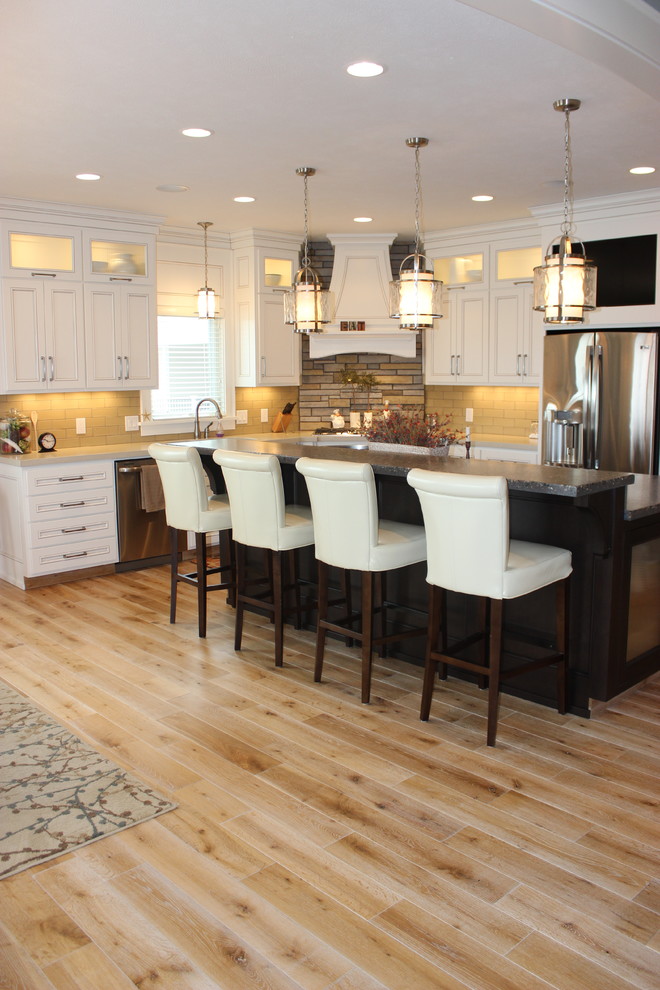 Photo of a mid-sized contemporary eat-in kitchen in Grand Rapids with white cabinets, beige splashback, stainless steel appliances, light hardwood floors and with island.