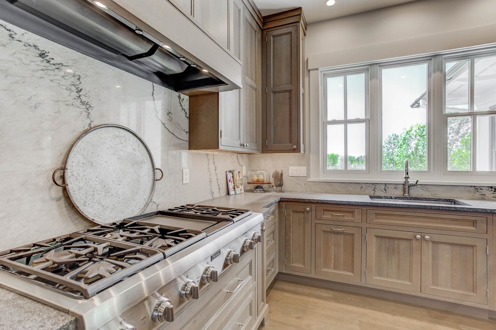 This is an example of an expansive transitional l-shaped open plan kitchen in Denver with an undermount sink, shaker cabinets, brown cabinets, white splashback, stainless steel appliances and with island.