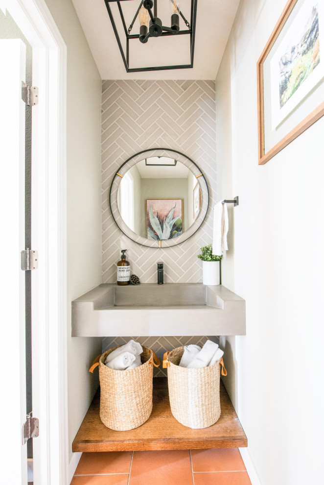 This is an example of a small contemporary powder room in Denver with gray tile, subway tile, terra-cotta floors, a wall-mount sink, concrete benchtops, orange floor, grey benchtops, a floating vanity and white walls.