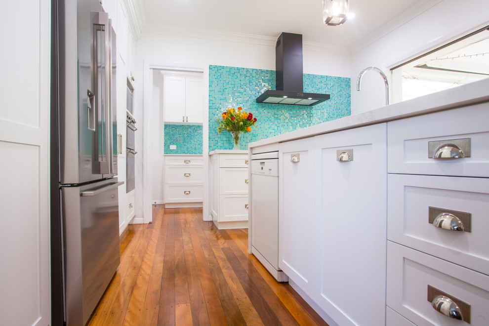 Example of a mid-sized minimalist l-shaped medium tone wood floor kitchen pantry design in Brisbane with a double-bowl sink, shaker cabinets, white cabinets, quartz countertops, blue backsplash, mosaic tile backsplash, stainless steel appliances, an island and white countertops