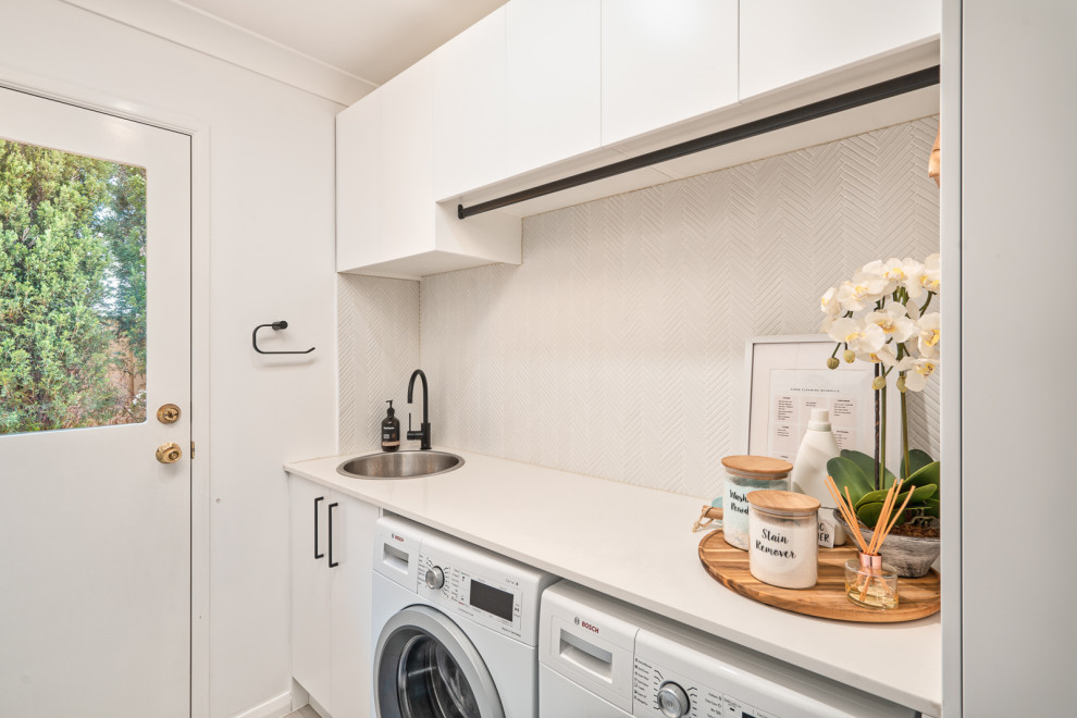 Inspiration for a mid-sized modern single-wall dedicated laundry room in Sydney with a drop-in sink, flat-panel cabinets, white cabinets, quartz benchtops, white splashback, ceramic splashback, white walls, ceramic floors, a side-by-side washer and dryer, beige floor and white benchtop.