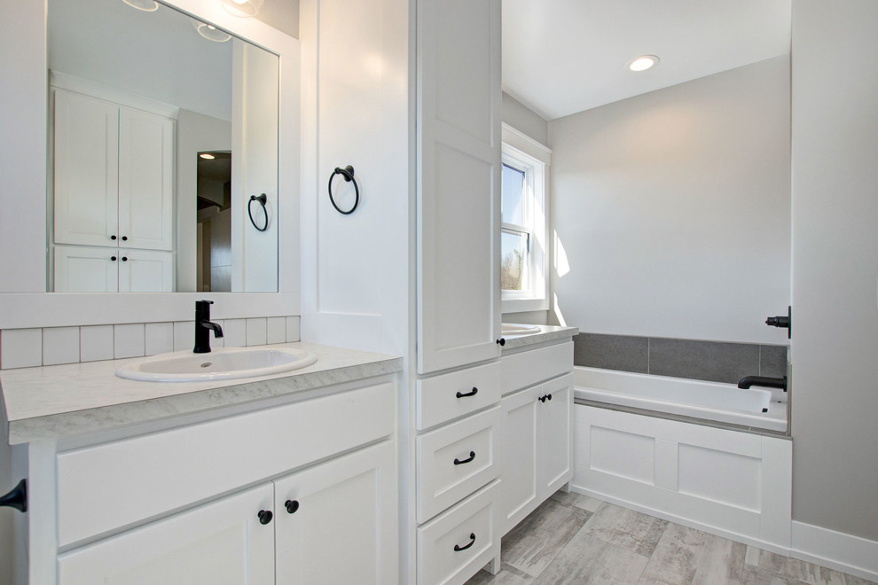Photo of a mid-sized contemporary master bathroom in Grand Rapids with shaker cabinets, white cabinets, a drop-in tub, an alcove shower, a two-piece toilet, gray tile, slate, grey walls, porcelain floors, a drop-in sink, beige floor, a hinged shower door and beige benchtops.