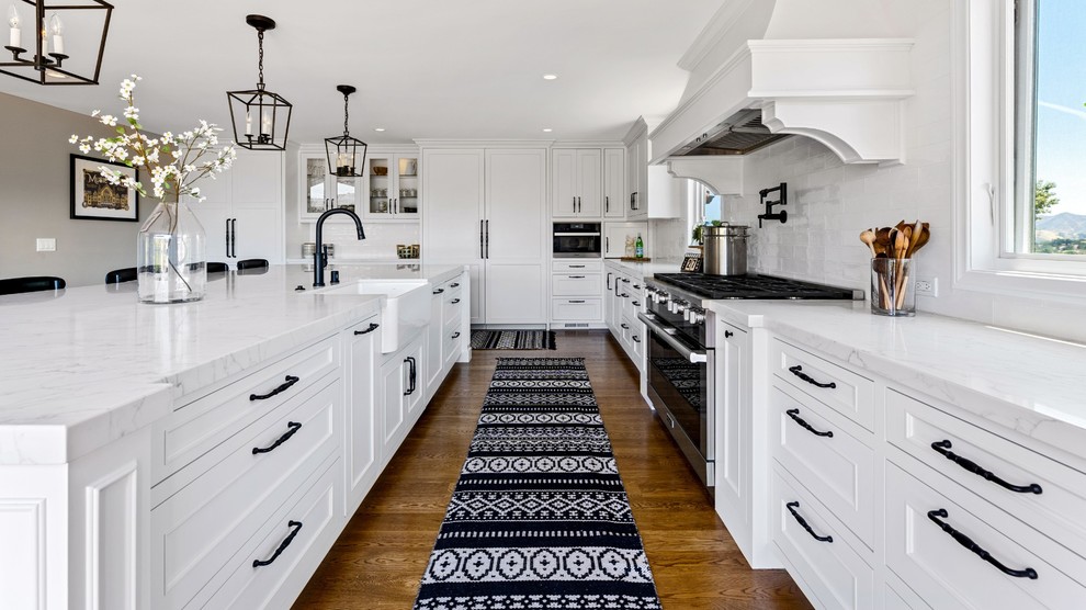 Example of a large transitional single-wall medium tone wood floor and brown floor eat-in kitchen design with a single-bowl sink, raised-panel cabinets, white cabinets, quartzite countertops, white backsplash, ceramic backsplash, stainless steel appliances, an island and white countertops