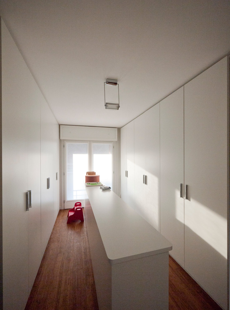 Design ideas for a large modern gender-neutral built-in wardrobe in Milan with flat-panel cabinets, white cabinets and bamboo floors.