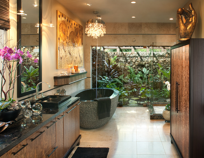 Design ideas for a mid-sized tropical master bathroom in San Diego with flat-panel cabinets, medium wood cabinets, a one-piece toilet, black tile, stone tile, beige walls, ceramic floors, a vessel sink, solid surface benchtops, a corner shower and a freestanding tub.