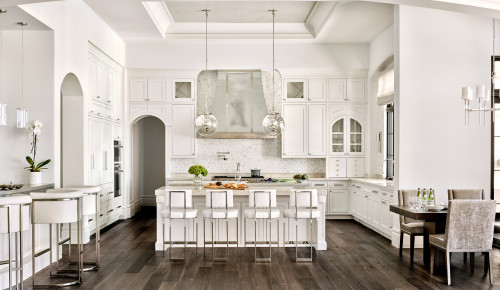 Spacious white kitchen with arched upper kitchen cabinets, a large central island and modern bar stools