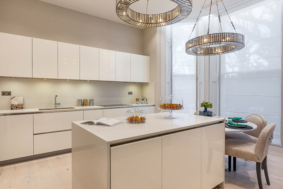 Inspiration for a contemporary kitchen in London with an undermount sink, flat-panel cabinets, white cabinets, white splashback, glass sheet splashback, light hardwood floors, with island and beige floor.