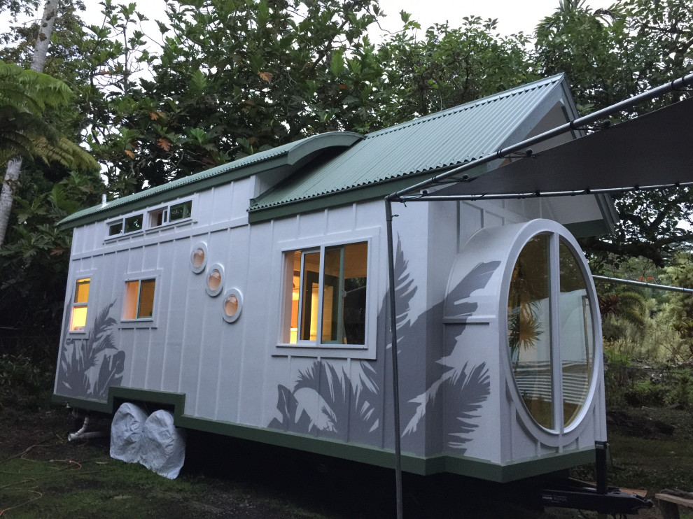 Photo of a small and white coastal two floor tiny house in Hawaii with wood cladding, a pitched roof, a metal roof, a grey roof and board and batten cladding.
