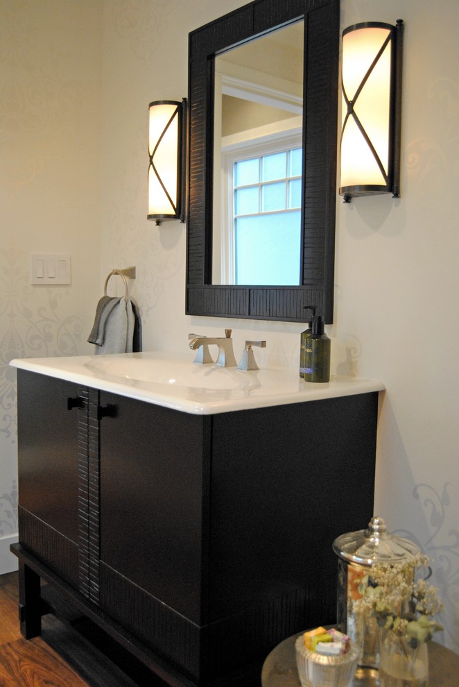 Photo of a mid-sized traditional powder room in Vancouver with an integrated sink, dark wood cabinets, solid surface benchtops, a two-piece toilet, white walls, medium hardwood floors and flat-panel cabinets.