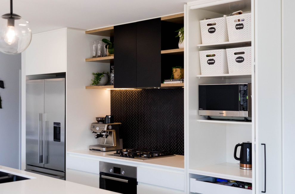 Design ideas for a mid-sized scandinavian galley eat-in kitchen in Auckland with a double-bowl sink, flat-panel cabinets, black cabinets, solid surface benchtops, black splashback, mosaic tile splashback, stainless steel appliances, porcelain floors, with island, grey floor and white benchtop.