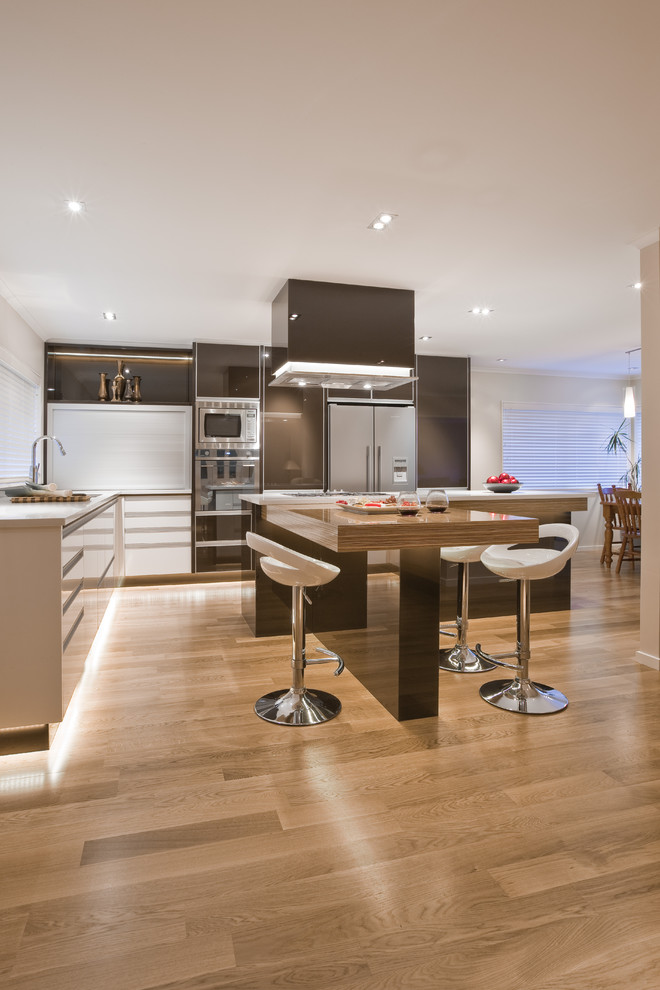 Photo of a large contemporary l-shaped eat-in kitchen in Los Angeles with flat-panel cabinets, brown cabinets, stainless steel appliances, an undermount sink, light hardwood floors and with island.