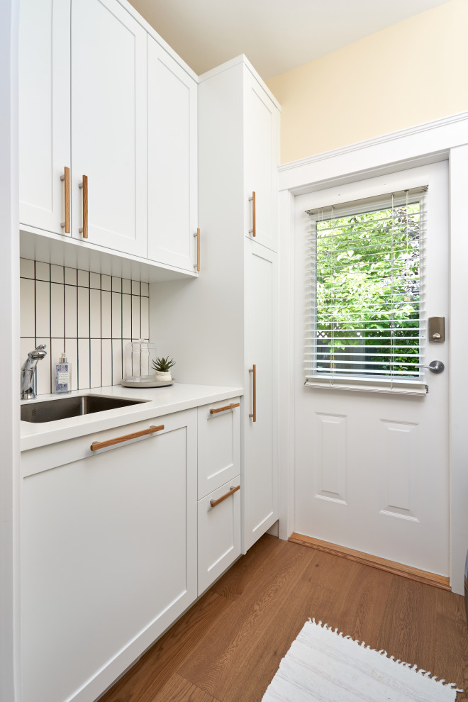 Inspiration for a small contemporary galley dedicated laundry room in Vancouver with an undermount sink, shaker cabinets, white cabinets, quartzite benchtops, white splashback, porcelain splashback, beige walls, light hardwood floors, a side-by-side washer and dryer and white benchtop.