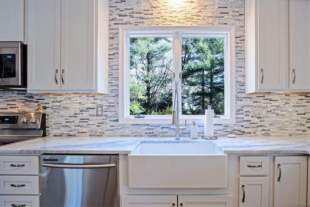 Design ideas for a large transitional l-shaped eat-in kitchen in Baltimore with a farmhouse sink, shaker cabinets, white cabinets, granite benchtops, grey splashback, stone tile splashback, stainless steel appliances, ceramic floors, no island, brown floor and white benchtop.