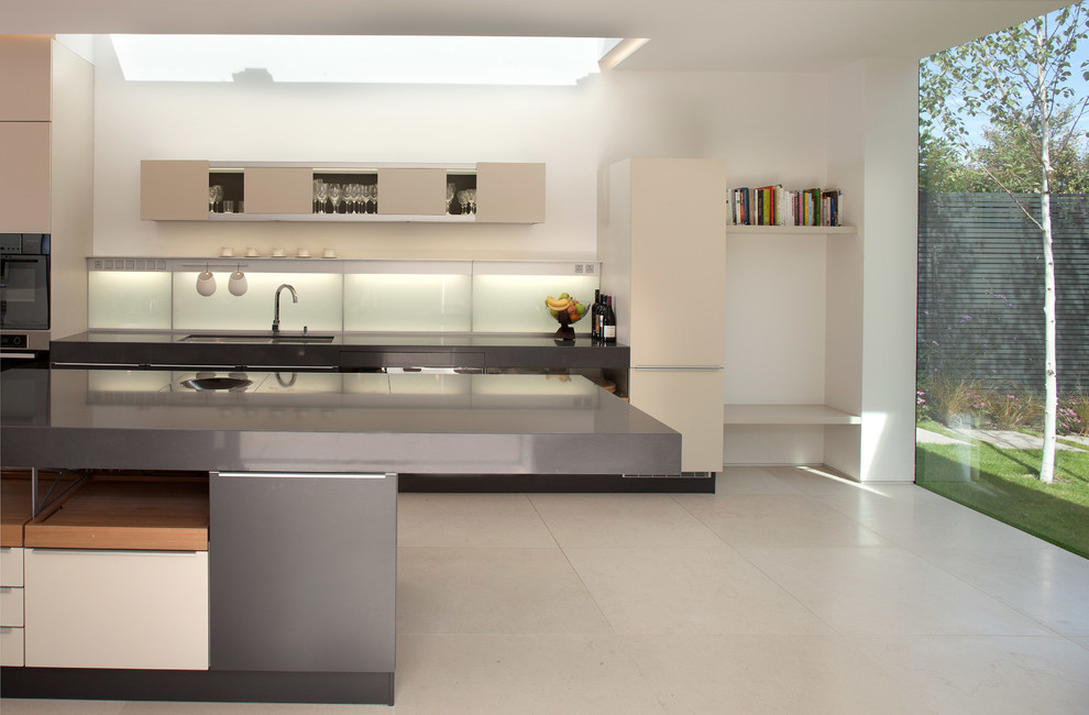 Photo of an expansive modern single-wall eat-in kitchen in Dublin with an integrated sink, flat-panel cabinets, white cabinets, solid surface benchtops, white splashback, glass sheet splashback, panelled appliances, limestone floors and with island.