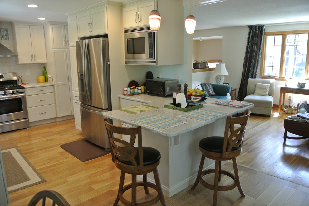 Inspiration for a transitional l-shaped medium tone wood floor eat-in kitchen remodel in Boston with an undermount sink, shaker cabinets, white cabinets, recycled glass countertops, white backsplash, subway tile backsplash, stainless steel appliances, a peninsula and white countertops