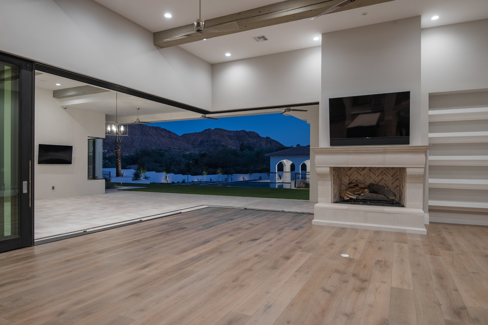 Large contemporary open concept living room in Phoenix with a library, medium hardwood floors, a standard fireplace, a stone fireplace surround, brown floor, grey walls and a wall-mounted tv.